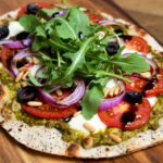 Pizza mit Pesto, Tomaten, Pinienkernen und Rucola
